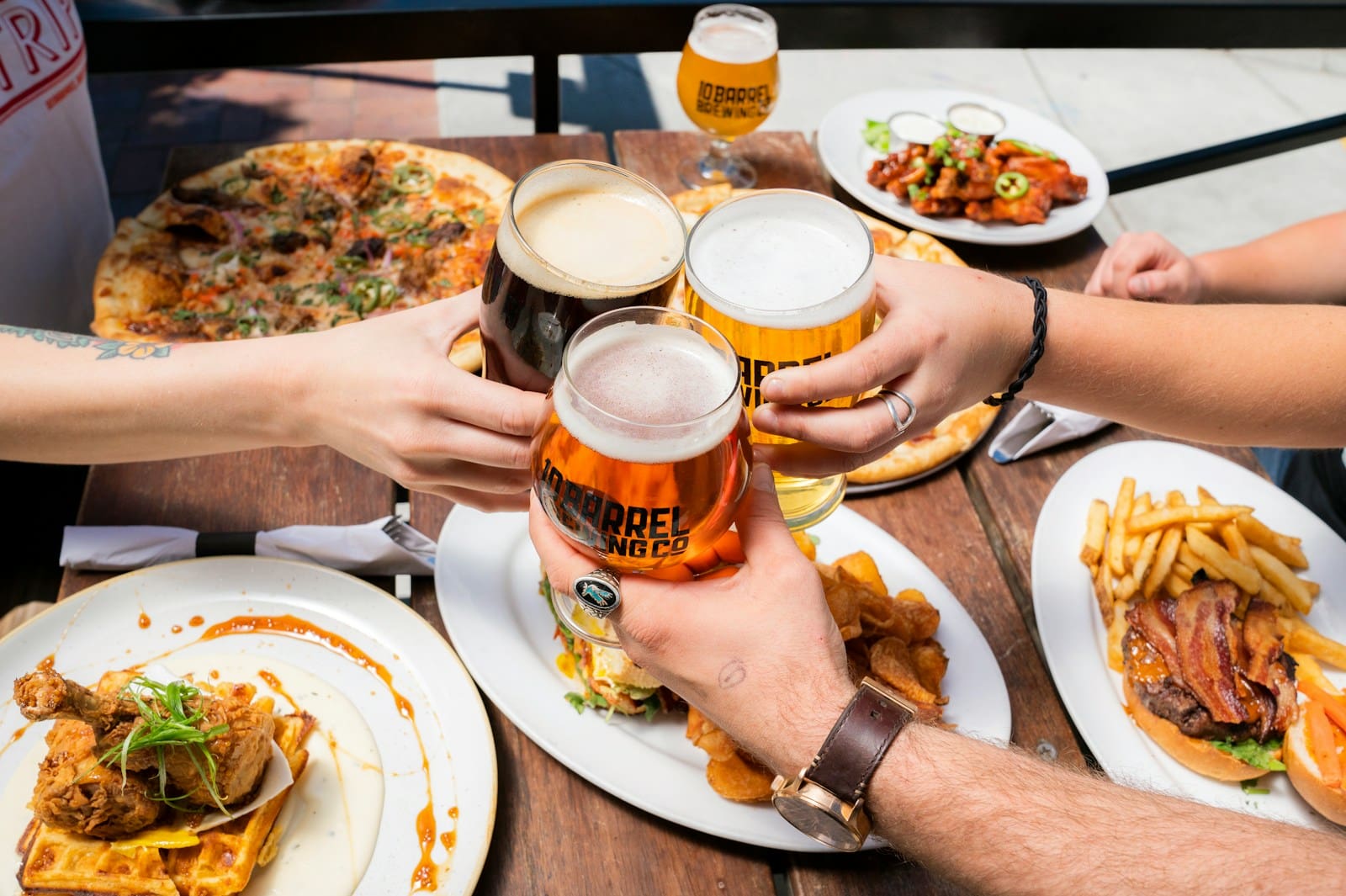 people having a toast of beers over plates of fun bar food