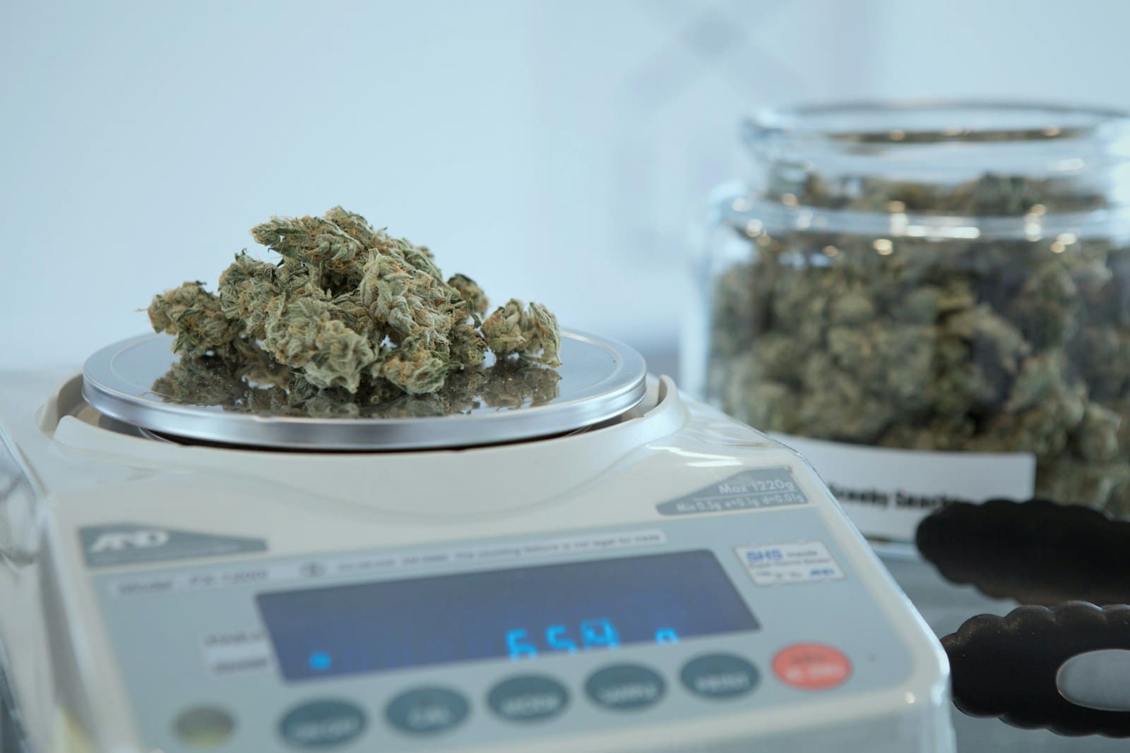 a gray and white scale measuring out marijuana by the ounce. A jar of buds or nugs sits alongside.