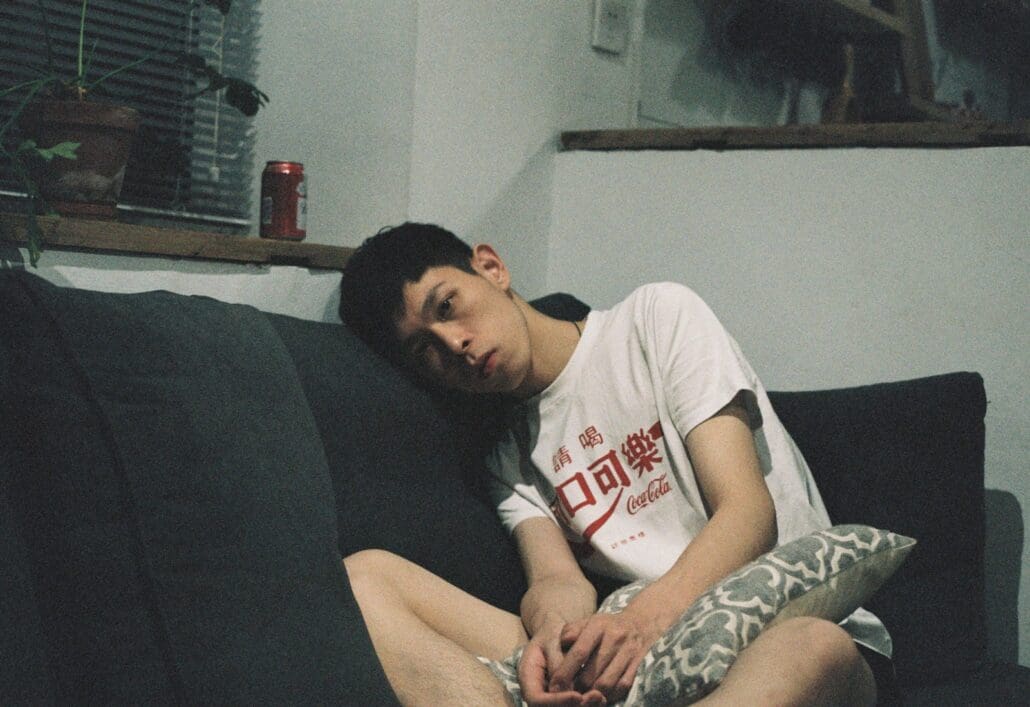 man in white T-shirt sitting on black couch looking groggy and dazed. Weed hangovers can linger the next day