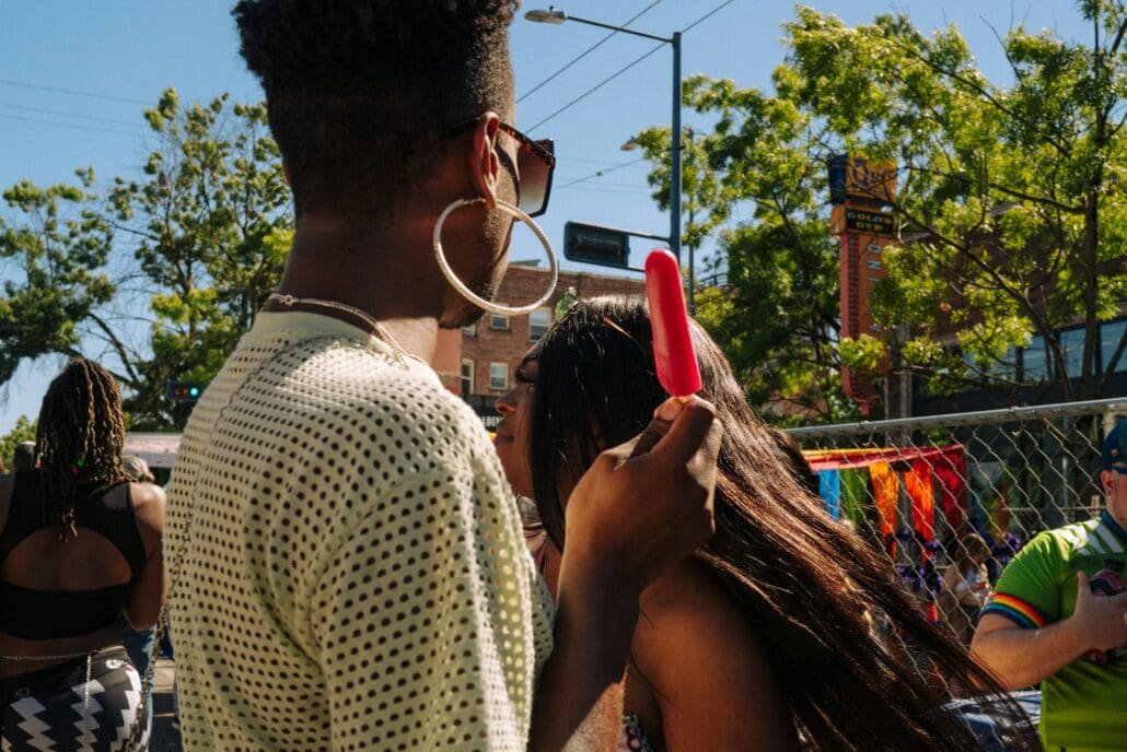 beautiful people walking on a sunny street in capitol hill. The lady in the foreground is holding a red popsicle and wears sunglasses. 