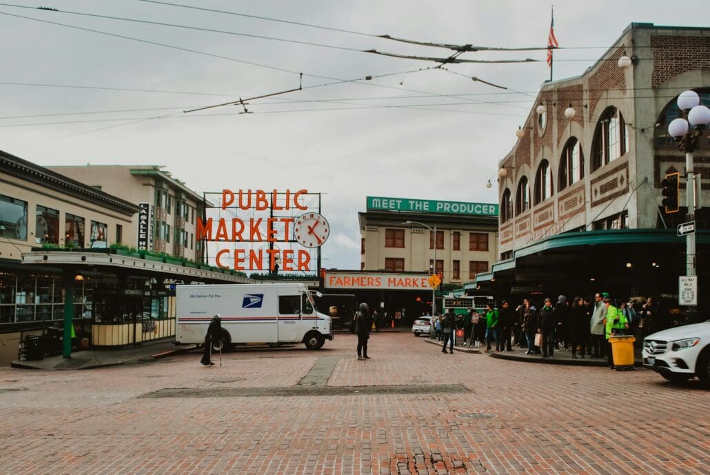 people walking on street during daytime the iconic pikes place market sign in the background, a white truck at the foreground