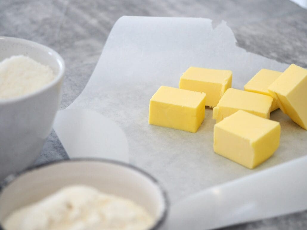 white ceramic bowl with white liquid, yellow butter cubes on parchment paper