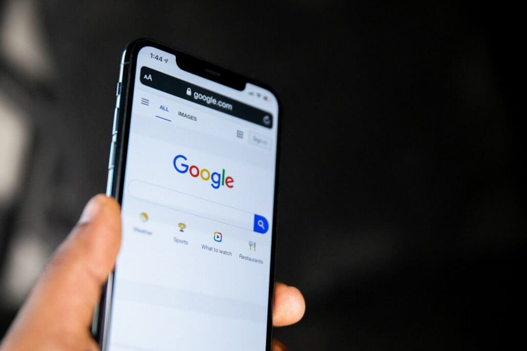 A hand holding a smartphone displaying the Google search engine homepage where you can access google reviews