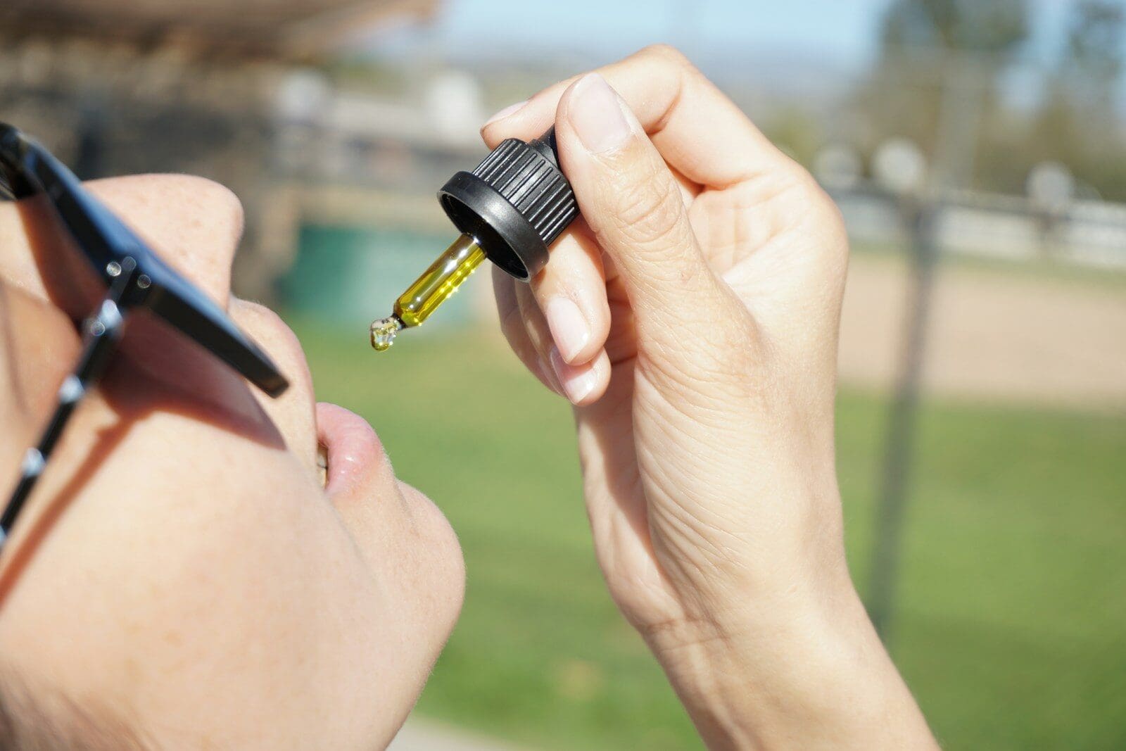 person holding black and yellow medicine dropper filled with CBD oil. CBD science is emerging with many health benefits
